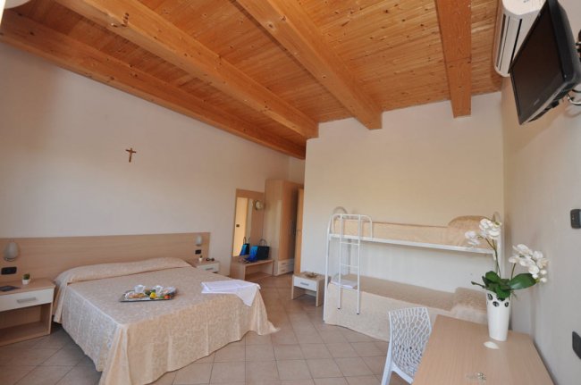 Camera con letto matrimoniale, letti a castello, travi in legno a vista e arredi semplici.