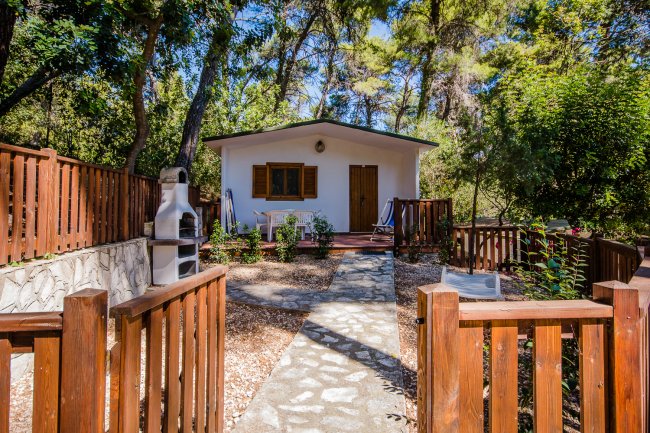 Una casa bianca con staccionata in legno, circondata da alberi, con un barbecue esterno.