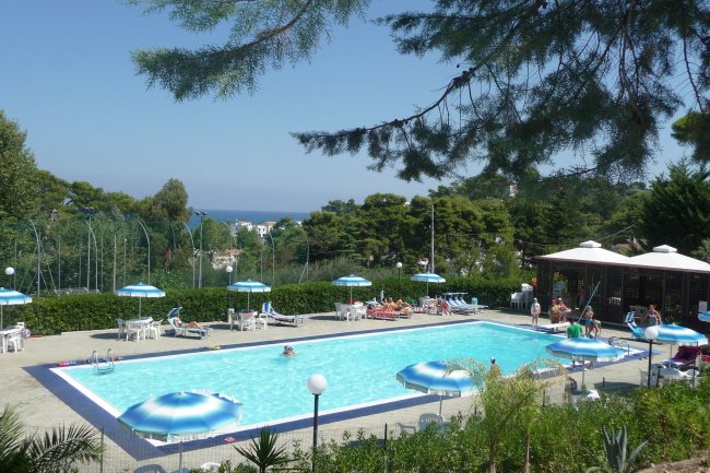 Piscina all'aperto circondata da ombrelloni e sedie a sdraio, con vista sul mare.