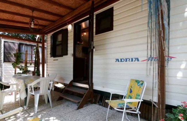 Roulotte con veranda arredata e sedie bianche.