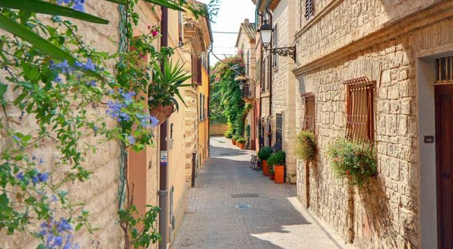 Stradina di un borgo con case in pietra e fiori appesi.