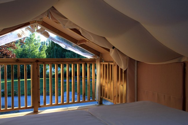 Interno di una tenda con vista su giardino alberato.