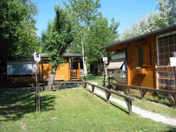 Bungalow di legno con veranda immersi nel verde, sentiero erboso al centro.