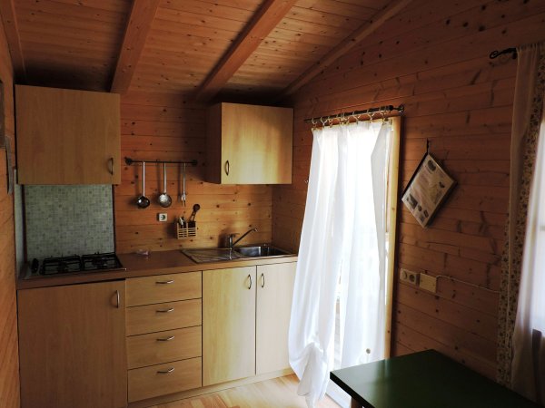 Cucina in legno chiaro con mobili, fornelli e tende bianche.