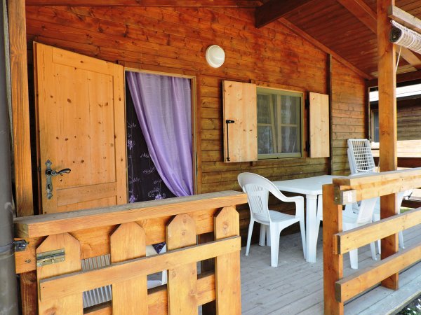 Veranda in legno con tavolo e sedie bianche, porta e finestre.