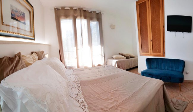 Stanza luminosa con letto, divano blu, mobili e TV a parete.