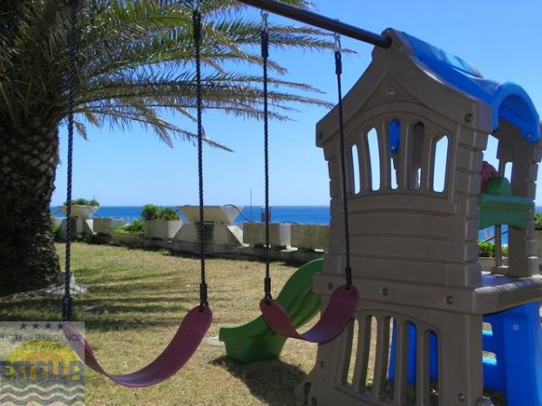 Altalene e scivolo in un giardino, vista mare sullo sfondo.