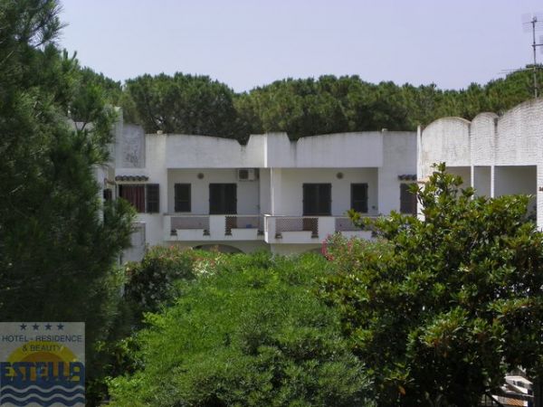 Edificio bianco a due piani, circondato da alberi verdi e arbusti.