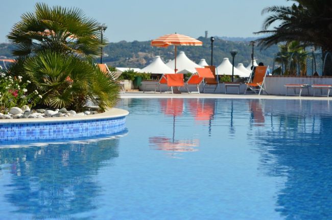 Una piscina con ombrelloni arancioni e palme sullo sfondo.