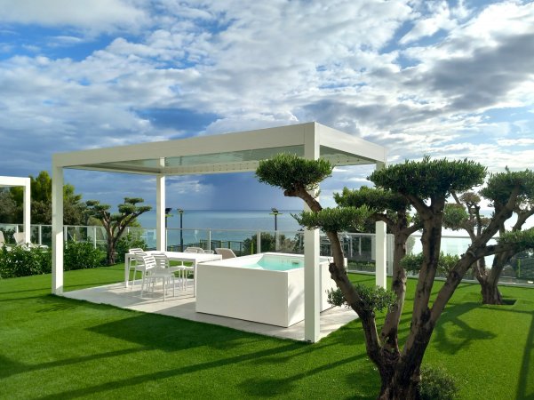 Una terrazza con pergola bianca e vista mare.