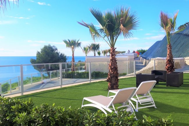 Due lettini bianchi su un prato con vista panoramica sul mare e palme.