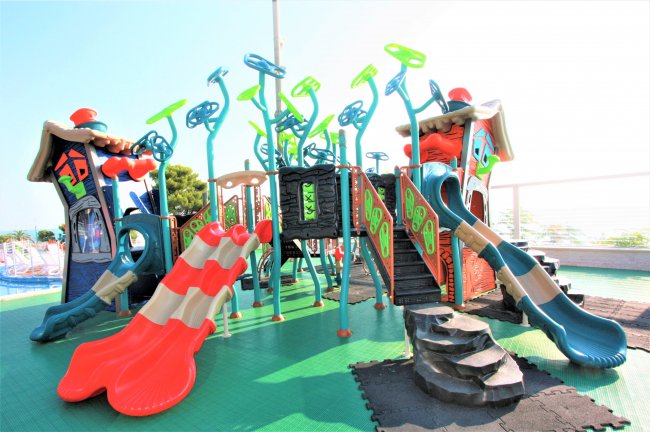 Un parco giochi colorato con scivoli rossi e blu su un pavimento verde.