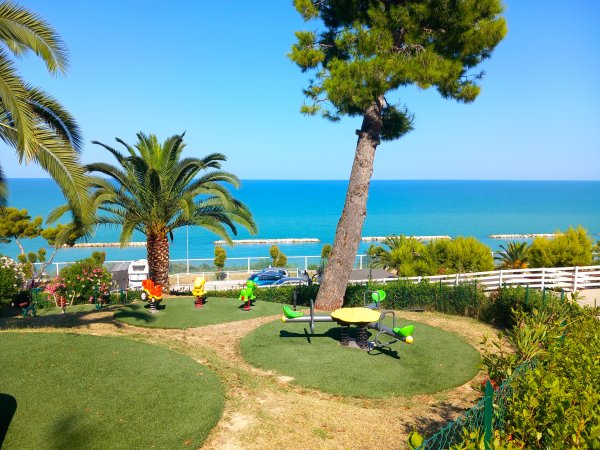 Giardino con altalene, palme e vista mare.
