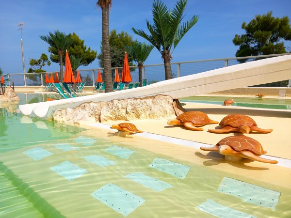 Piscina con statue di tartarughe, palme, e sedie a sdraio arancioni.