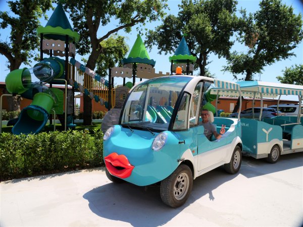 Un'auto elettrica decorata con una faccia felice vicino a un parco giochi con scivoli verdi.
