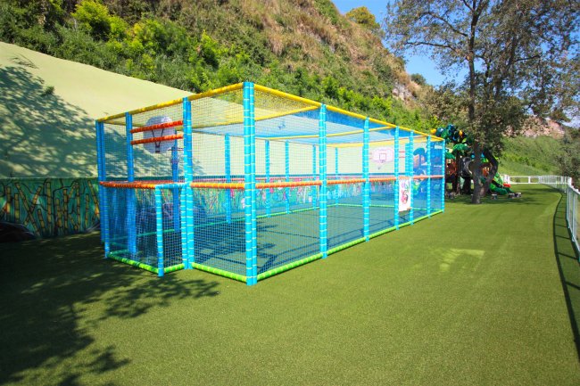 Un campo da gioco per bambini recintato con struttura colorata, su prato verde.