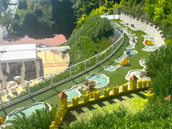 Un percorso da minigolf con decorazioni gialle su erba sintetica e arbusti.