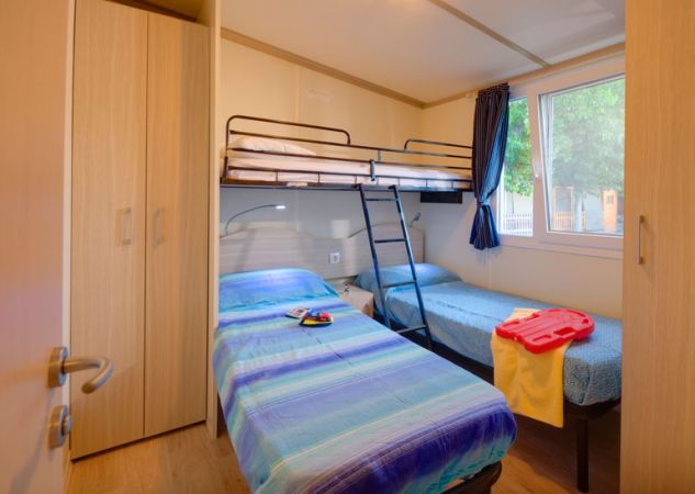 Camera con letto singolo, letto a castello, armadio e finestra. Copriletto blu e giochi sul letto.