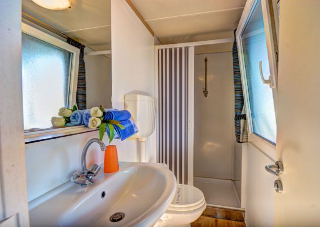 Bagno con lavandino, doccia, WC, finestra e asciugamani colorati vicino al lavandino.