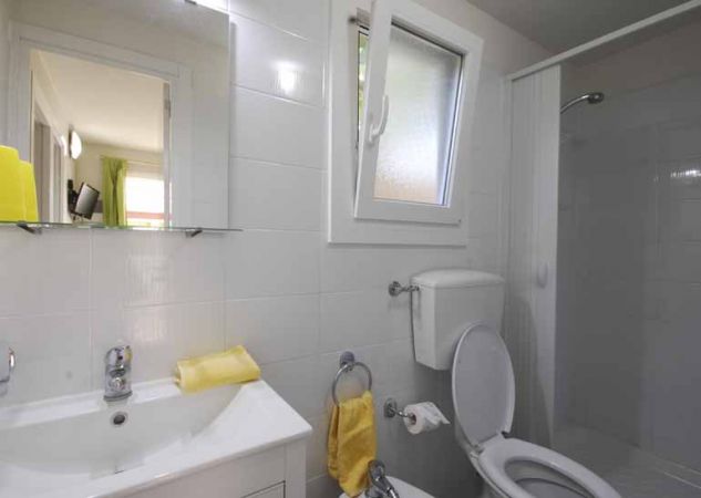 Bagno con wc, lavabo, specchio e asciugamani gialli. Finestre e doccia presenti.