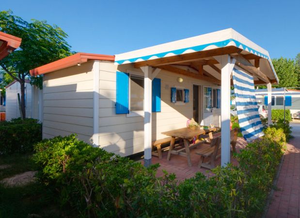 Un bungalow con persiane blu e veranda coperta, circondato da piante.