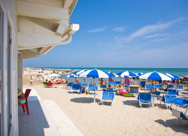 Lettini e ombrelloni blu su spiaggia assolata.