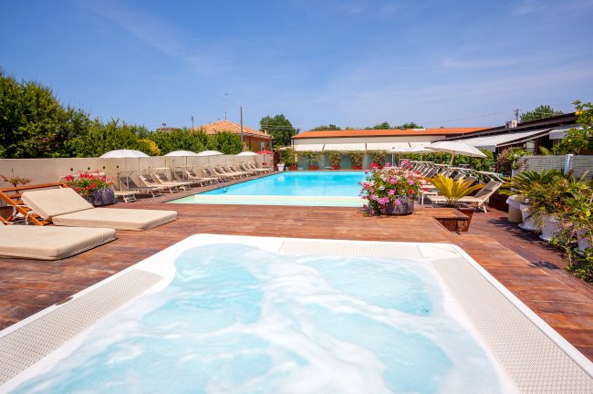 Piscina all'aperto con idromassaggio, lettini e ombrelloni, circondata da piante.