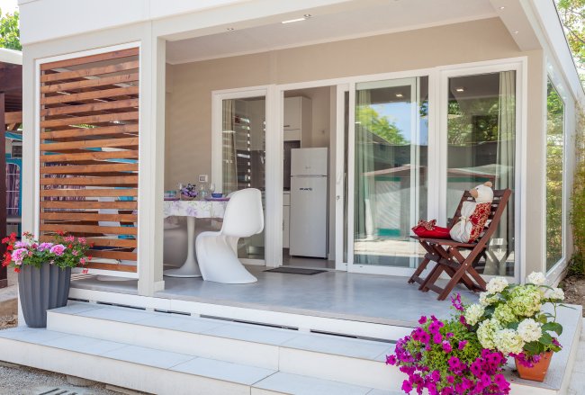 Veranda con tavolino, sedie e fiori colorati davanti a una porta vetrata.
