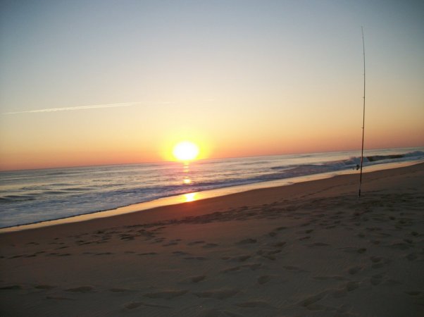 Un tramonto su una spiaggia sabbiosa con canna da pesca piantata nella sabbia.