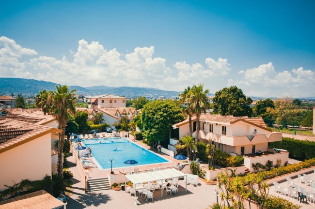 Villette con piscina, palme e colline sullo sfondo.