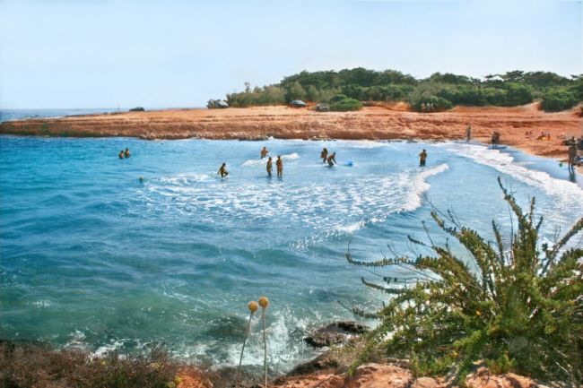 Spiaggia sabbiosa con persone che nuotano in una baia.