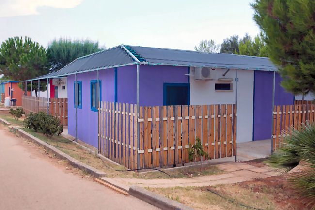 Casa viola con recinzione in legno su una strada alberata.