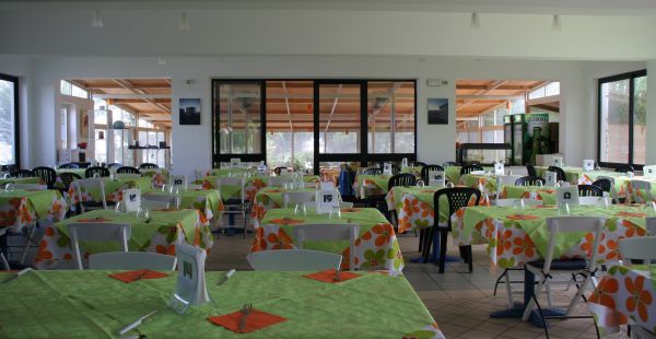Un'ampia sala da pranzo con tovaglie verdi e motivi floreali, tavoli numerati.