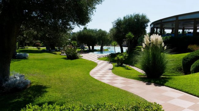 Sentiero curvo tra prati e alberi, vicino a una piscina.