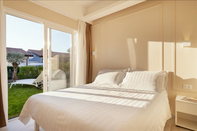 Camera da letto luminosa con un letto matrimoniale e porta finestra che si apre su un giardino.