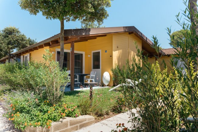 Bungalow giallo con veranda in un giardino fiorito.