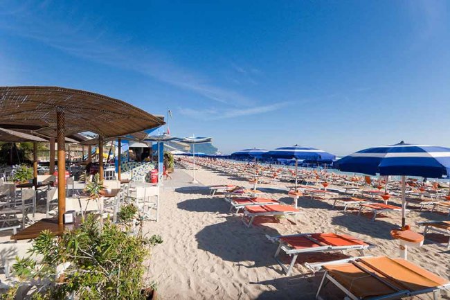 Spiaggia con sdraio e ombrelloni blu e bianchi su sabbia chiara.