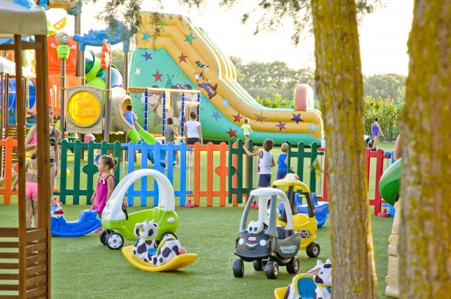 Parco giochi con bambini, automobili giocattolo e uno scivolo gonfiabile colorato.