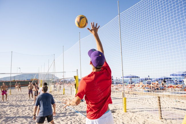 Un uomo gioca a beach volley sulla spiaggia, alza la palla per un attacco.