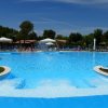 Piscina azzurra con giochi d'acqua, ombrelloni e persone intorno.