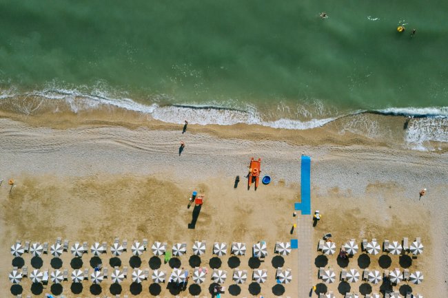 Veduta aerea di una spiaggia con ombrelloni allineati e mare calmo.