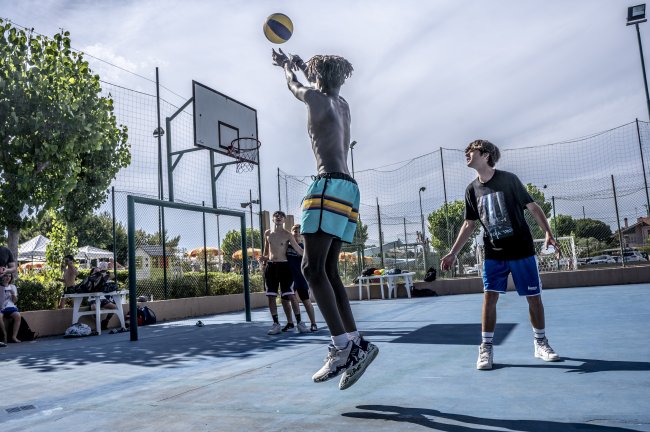 Ragazzi giocano a basket all'aperto, uno in salto tenta un tiro sotto il canestro.