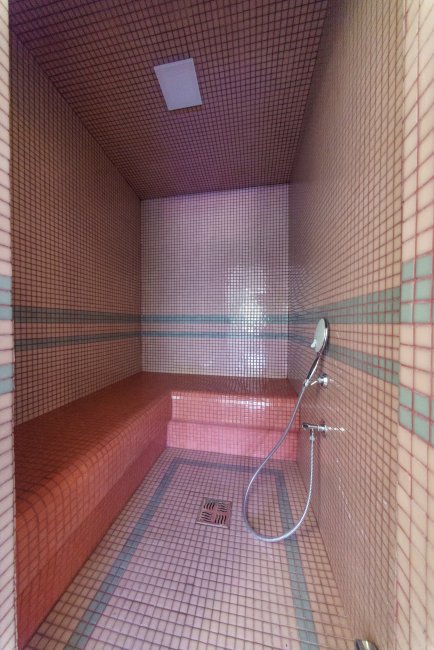 Interno di un bagno turco con piastrelle rosse e blu, doccia a mano e sedile integrato.