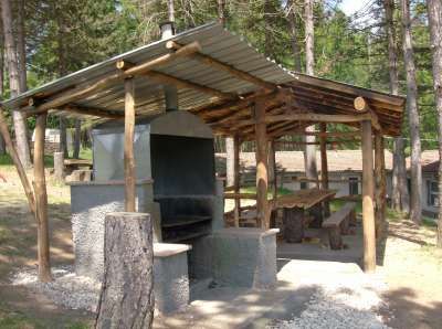 Area barbecue coperta con un tavolo e panche di legno.