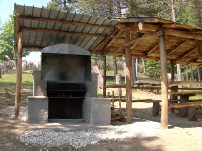 Barbecue in muratura accanto a tavoli da picnic coperti in un'area verde.