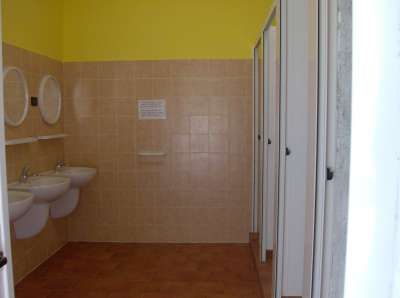 Bagno con lavandini bianchi, specchi tondi e pareti piastrellate beige.
