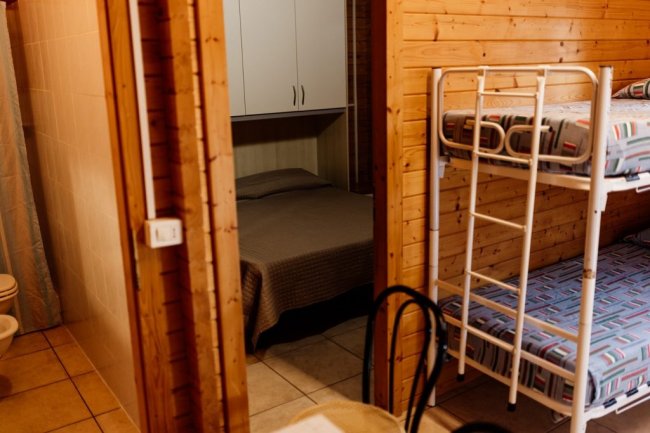 Interno di una casetta con letto matrimoniale e letti a castello.