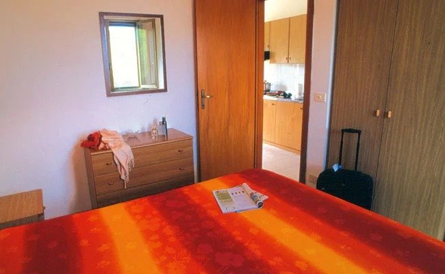 Camera con letto colorato, cassettone e vista su cucina.