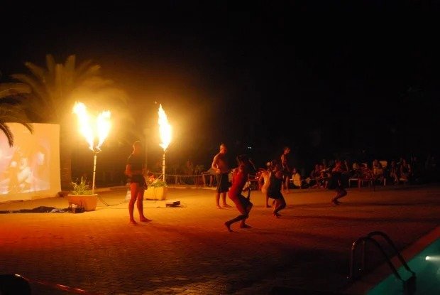 Artisti eseguono uno spettacolo di fuoco di notte, con pubblico sullo sfondo.