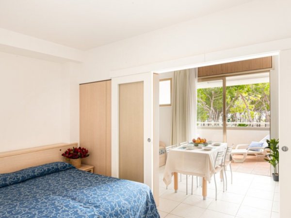 Appartamento con letto matrimoniale, tavolo da pranzo e vista su balcone verde.